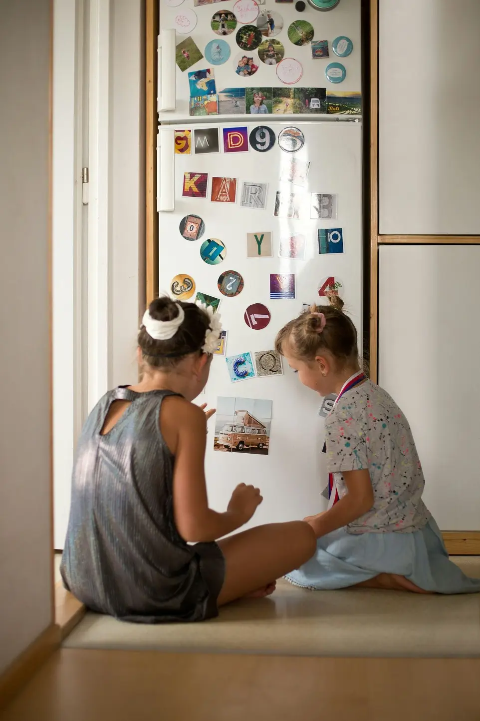 two young girls sitting on the floor looking at a refrigerator