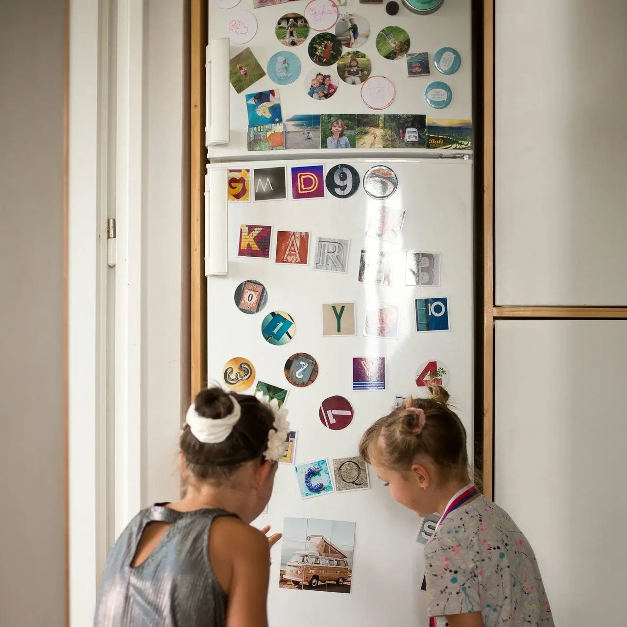 two young girls sitting on the floor looking at a refrigerator